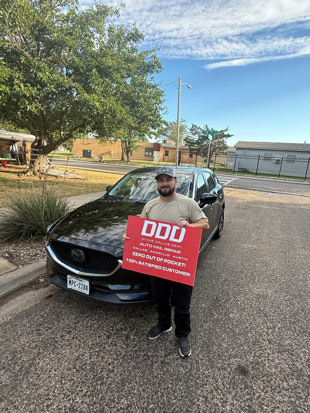 Customer with a Divine Dallas Dent sign next to a black Mazda CX-5 after hail repair