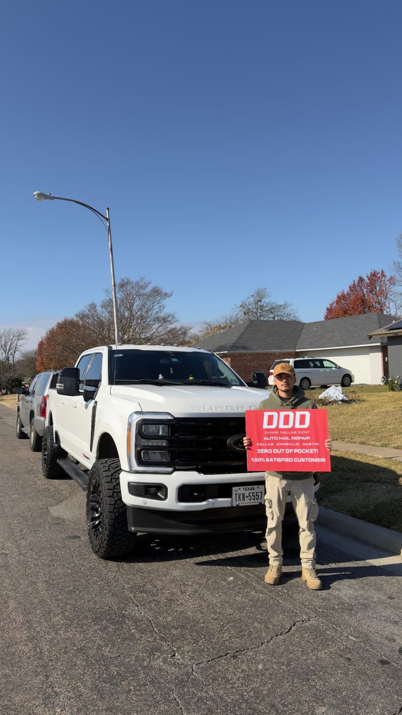 Customer with a Divine Dallas Dent sign beside a white Ford Super Duty after hail repair